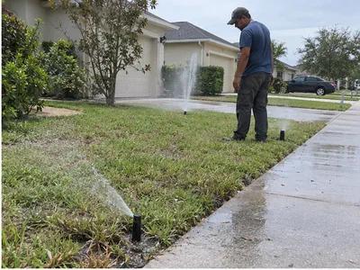 Technician watching uneven spray patterns while testing a sprinkler zone beside a Kissimmee driveway