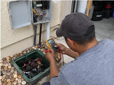 Technician testing valve wiring with a multimeter beside an open irrigation controller